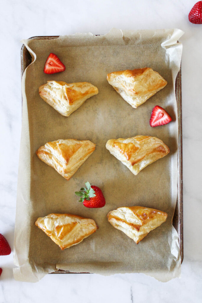 Cooked puff pastry dough is on a baking sheet lined with brown parchment paper. 