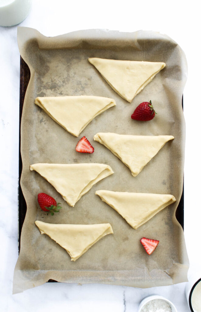 Puff pastry dough is folded and placed on a baking sheet lined with brown parchment paper. 