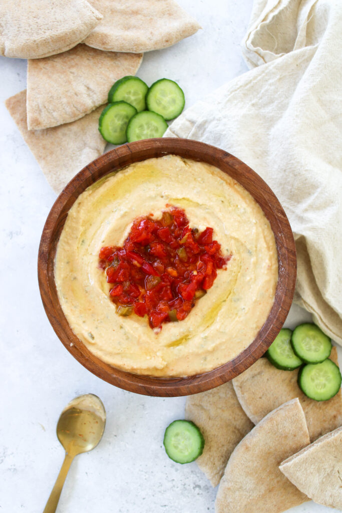 Homemade spicy hummus in a wooden bowl with sliced whole wheat pita bread and sliced cucumbers