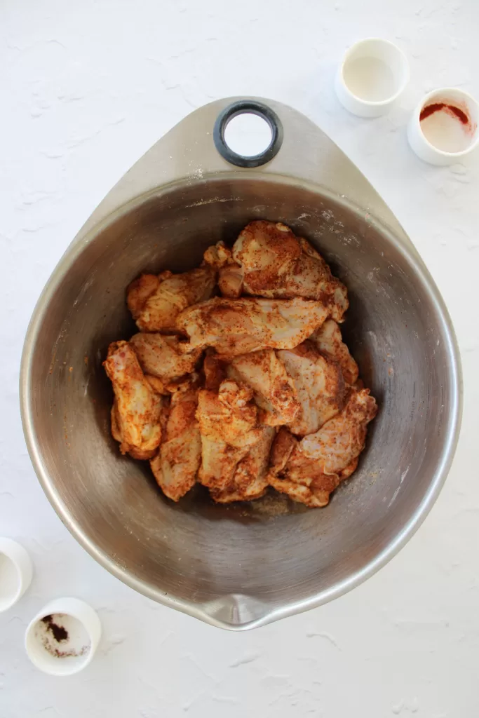Raw chicken wings tossed in cornstarch and spices in a stainless steel bowl. 