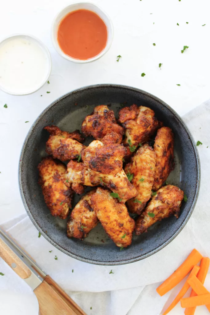 Crispy cornstarch chicken wings in a stone bowl surrounded by ranch dressing, buffalo sauce, and carrots. 