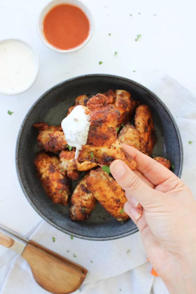 Crispy cornstarch chicken wings in a stone bowl. One chicken wing being held and dipped in ranch dressing. 