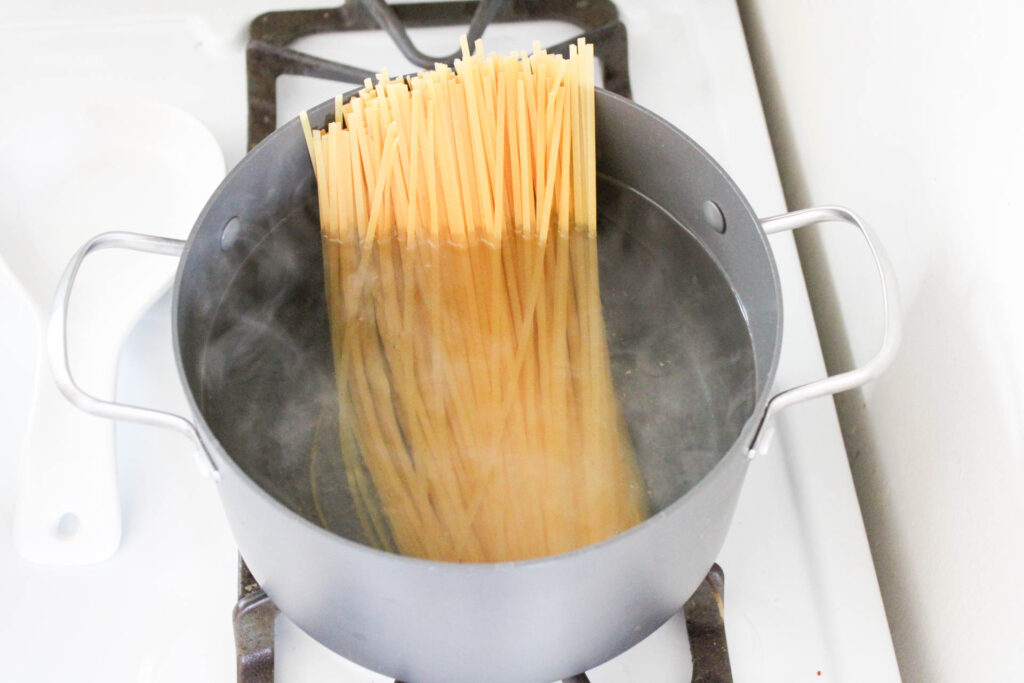 Linguini pasta noodles in a bowl of boiling water on a white stove top. 