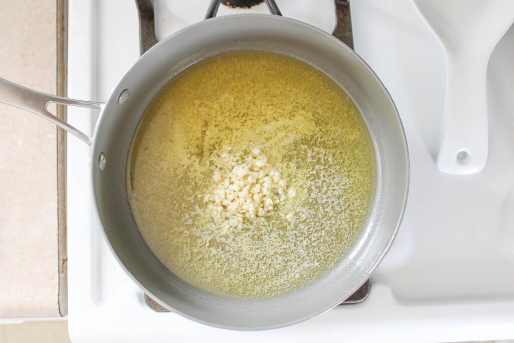 Melted butter and minced garlic in a gray pan on a white stove top.