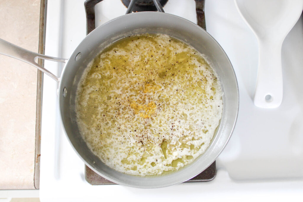 garlic lemon white wine pasta sauce in a gray pan on a white stove top. 