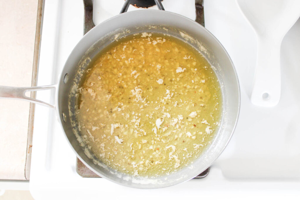 Butter, white wine, and garlic in a gray pan on a white stop top. 