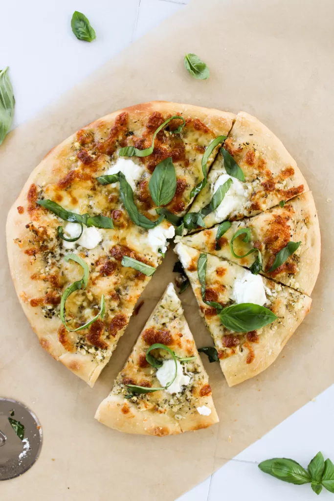 Sliced olive oil pizza without tomato sauce topped with fresh basil and three cheeses
