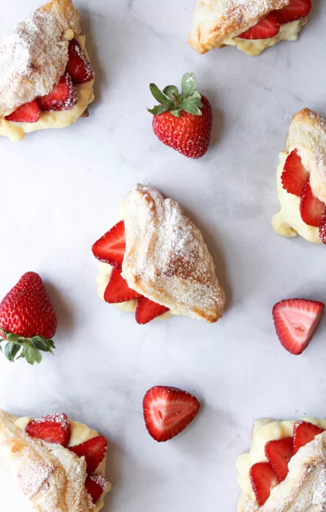 Several strawberry croissants arranged on a marble counter with strawberries and powdered sugar. 