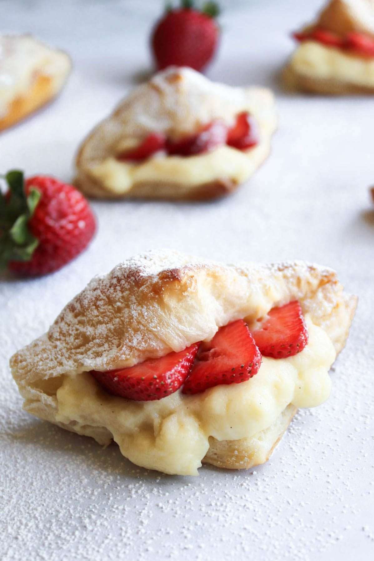 Strawberry and custard stuffed croissant with more in the background on a marble surface.