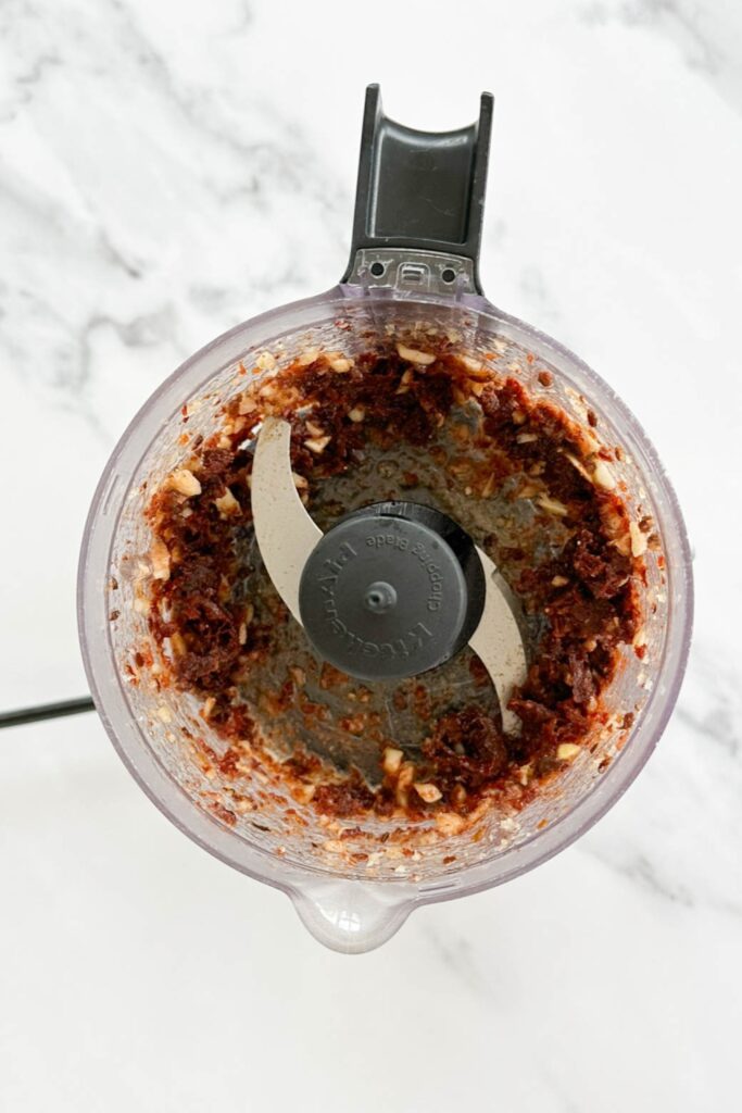 sun-dried tomato spread in the bowl of a small food processor on a marble counter top. 