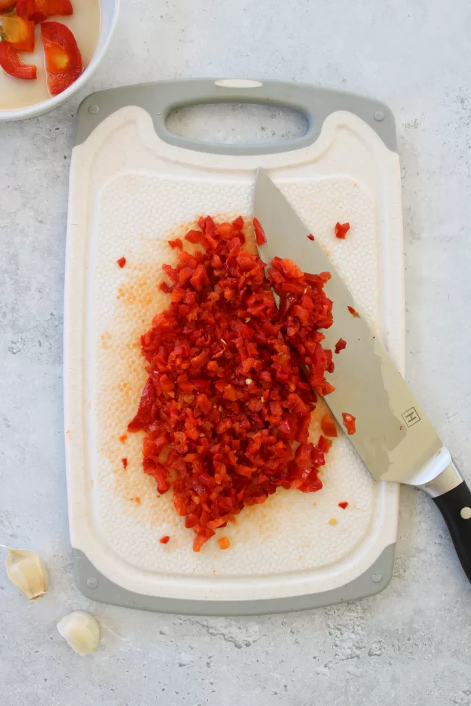 Diced cherry peppers on a cutting board with a knife